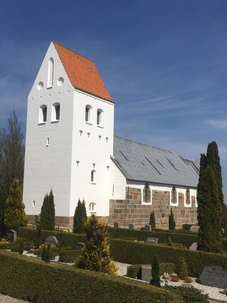 Hvidkalket landsbykirke med rødt tag på tårnet