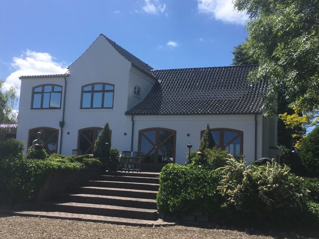 Hvidpudset villa med sort tegltag og bred trappe op gennem haven