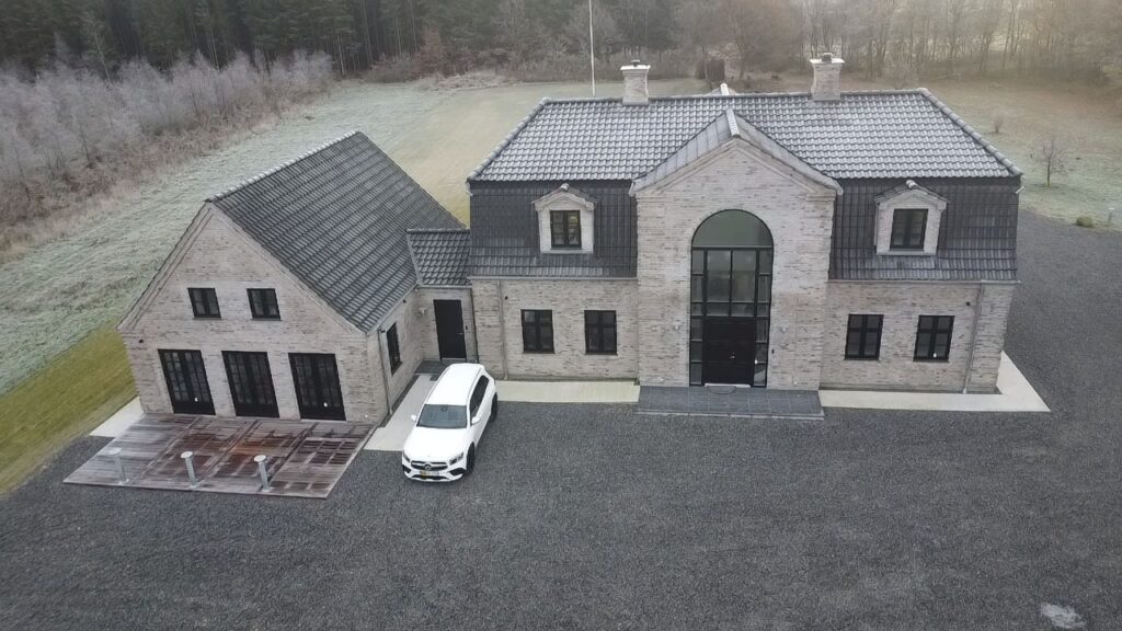 Ny villa i lyse mursten med buet indgangsparti og indkørsel, set fra luften