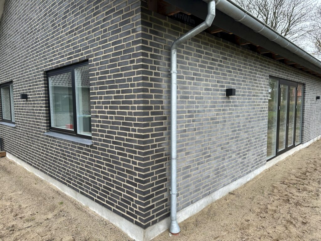 Hjørne af nyt hus i grå mursten med store vinduespartier
