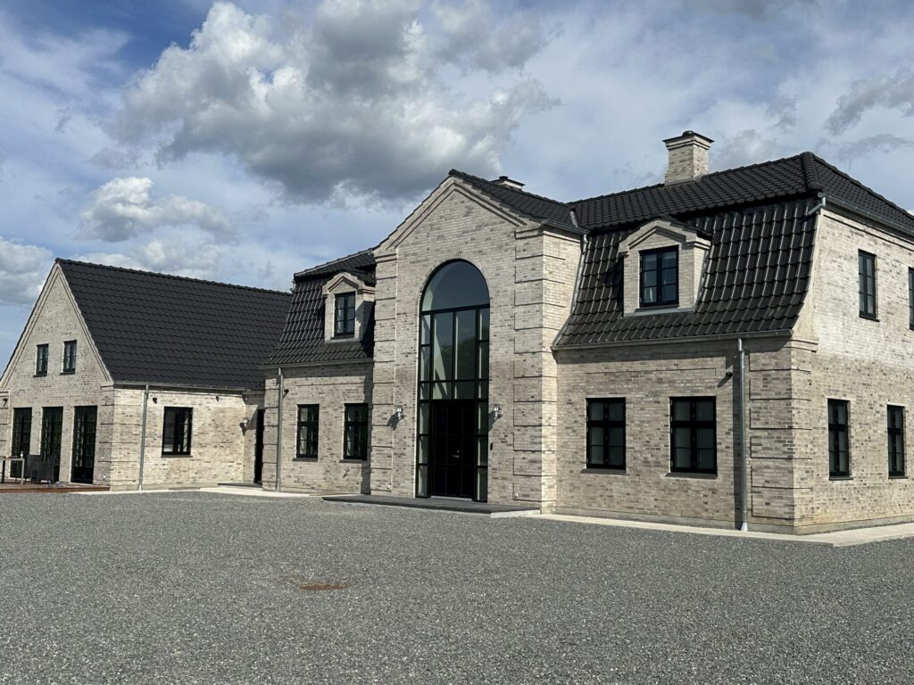Ny villa i lyse mursten med højt buet glasparti ved indgangen og sort tegltag